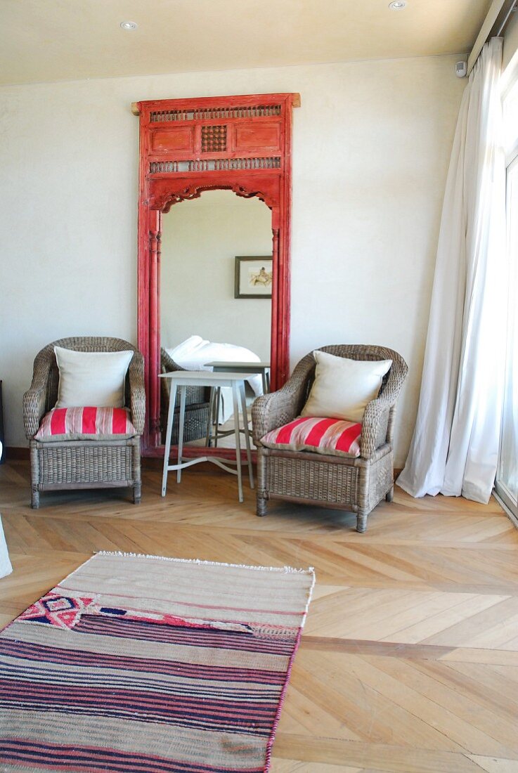 Gemütliche Ecke im Schlafzimmer mit zwei Korbstühlen beidseits eines Spiegels mit verziertem Holzrahmen
