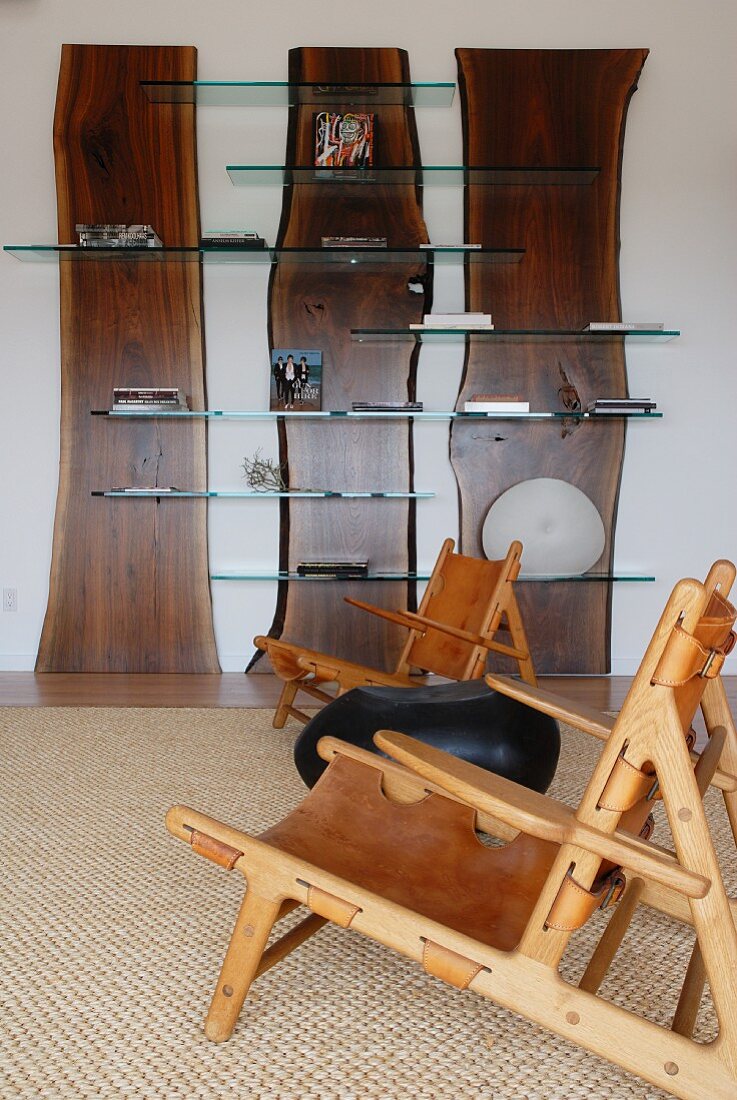 Baumstamm-Schichten mit Glasborden als kreatives Wandregal und Holzsessel mit Lederbespannung in grosszügigem Wohnraum