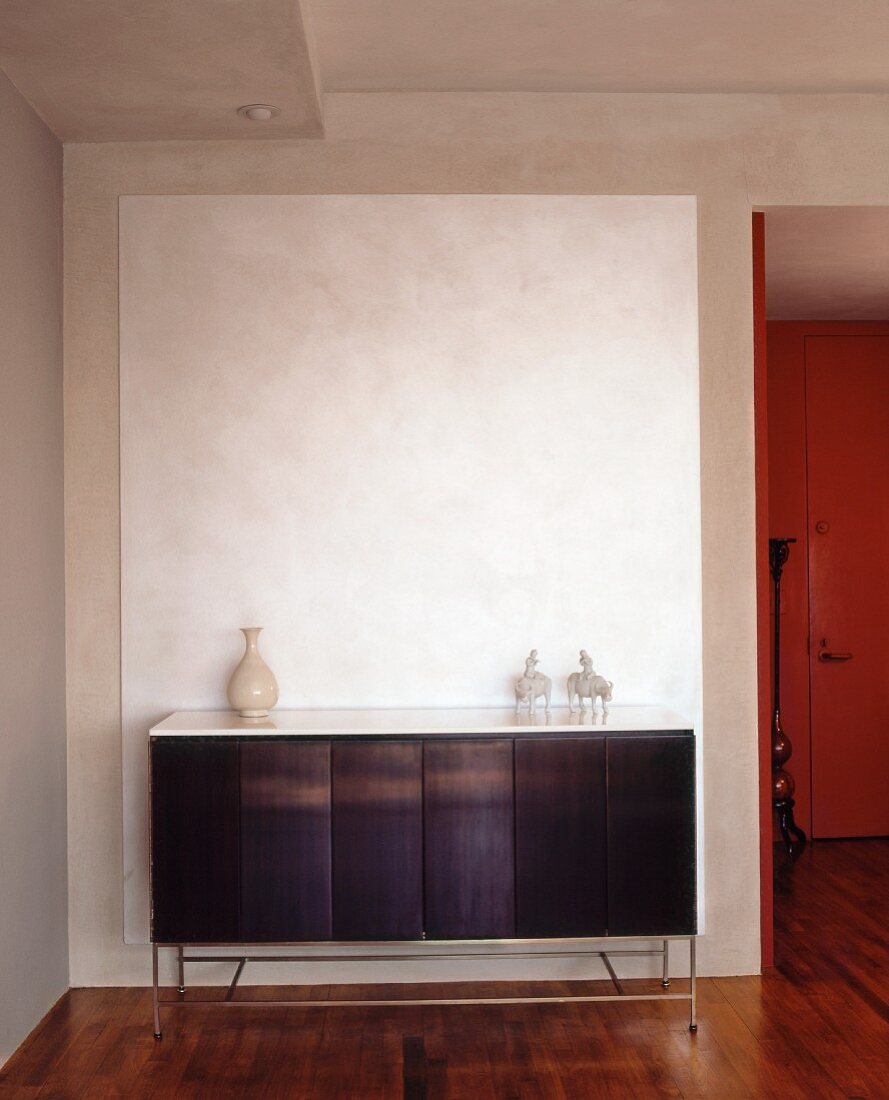 Weisses Farbfeld auf Sichtbetonwand hinter sparsam dekoriertem Sideboard