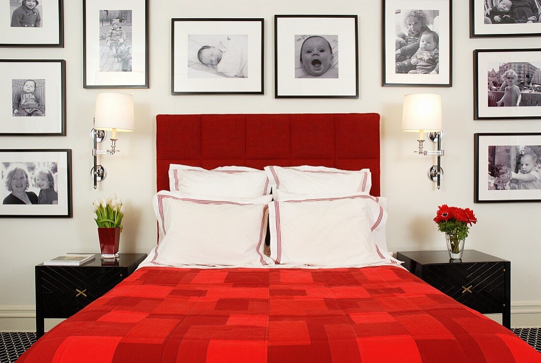 Red double bed framed by large collection of black and white photographs