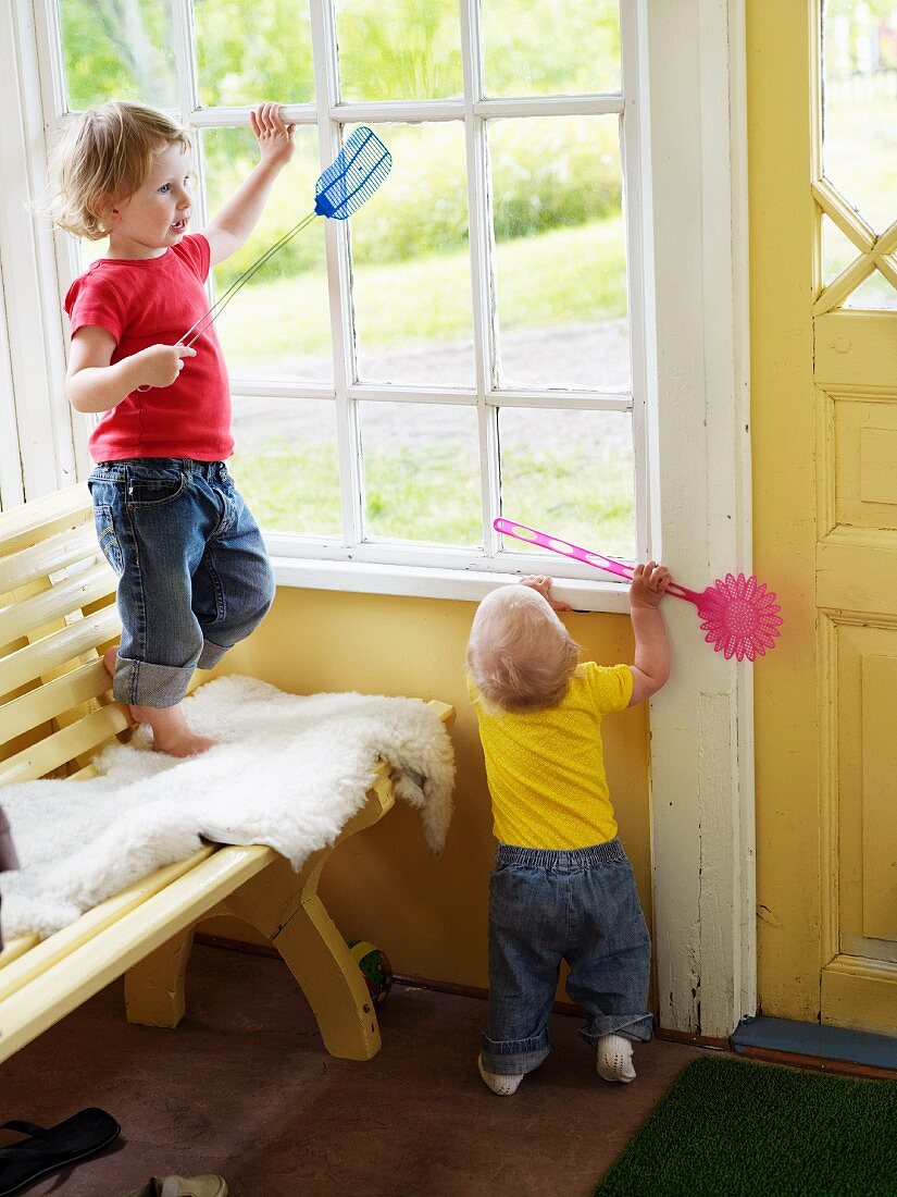 Zwei kleine Kinder spielen mit Fliegenklatschen auf Veranda