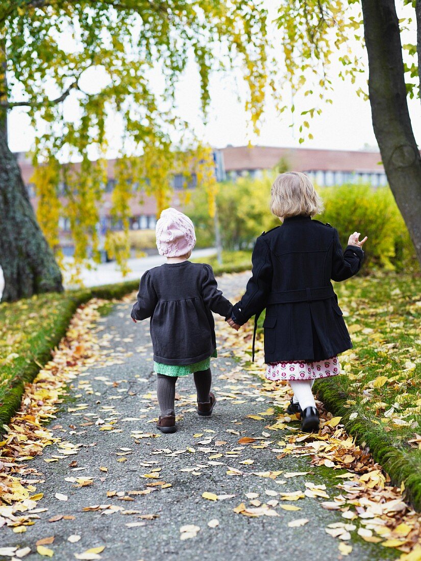 Two children wearing winter coats walking along path holding hands