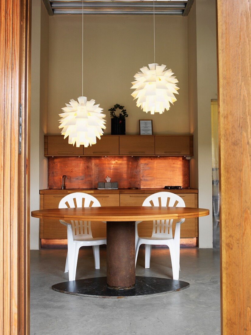 Blick auf Küchenzeile mit kupferfarbener Rückwand, rundem Esstisch & zwei modernen Hängeleuchten