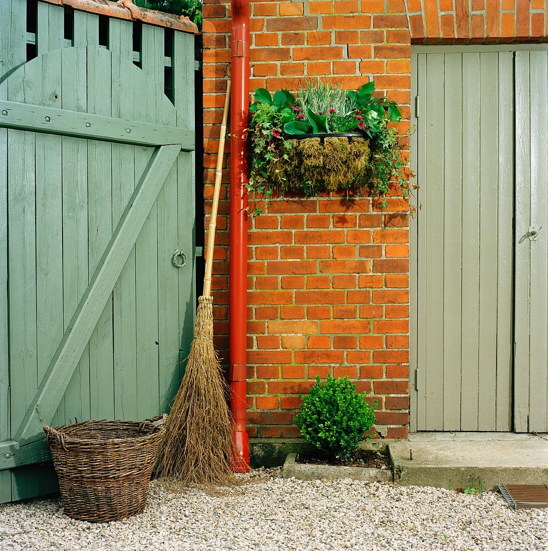 Besom broom, wicker basket & manger basket planted with autumnal arrangement on house facade
