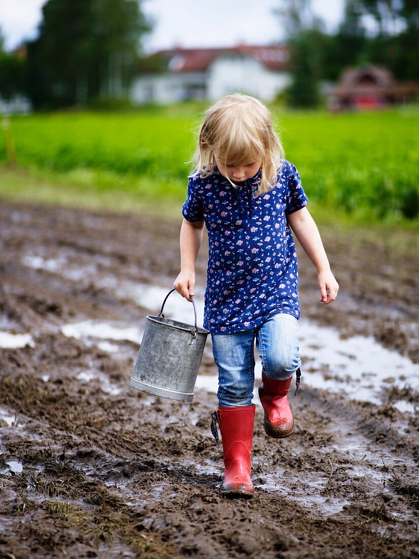 Little girl holding bucket playing in mud