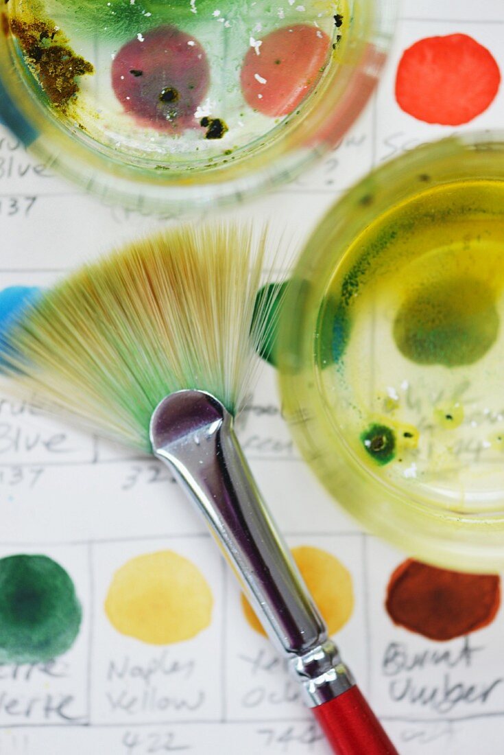 Wassergläser mit Farbpinsel und selbstgemalten beschrifteten Farbmustern