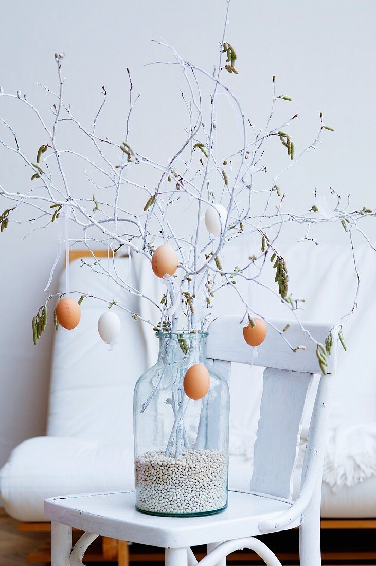 Osterstrauss aus weiss bemalten Frühlingszweigen mit daran hängenden ausgeblasenen Eiern in großer Glasvase