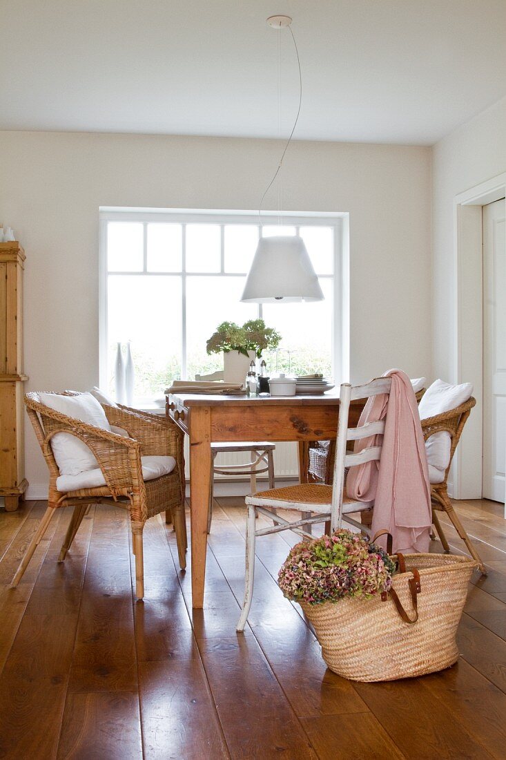 Wooden table, wicker chairs and white-painted cane chairs below pendant lamp