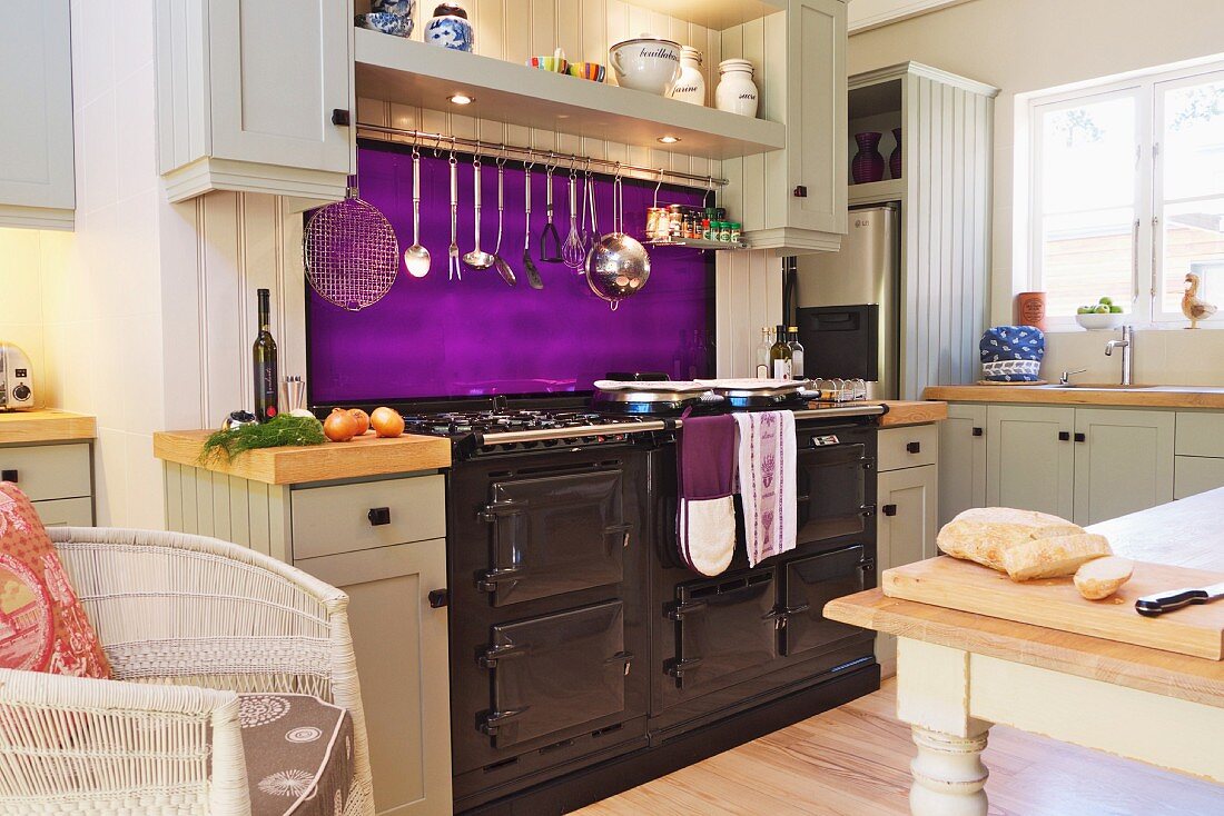 weiße Küche im Landhausstil mit leuchtend violettem Spritzschutz und großem Herd mit Metallfront