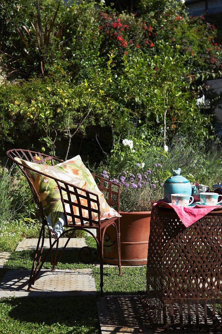 Sonniger Gartenplatz mit Gartenmöbeln aus Metall und Boden im Schachbrettmuster; auf dem Tisch Teekanne und Teetassen