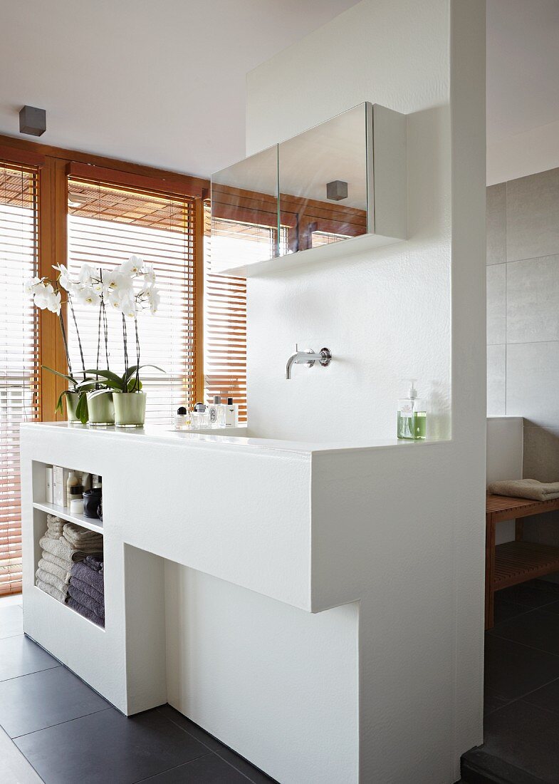 Weisses Trennelement als Waschtisch, Waschbecken und Regal vor Fensterfront mit Holzjalousien