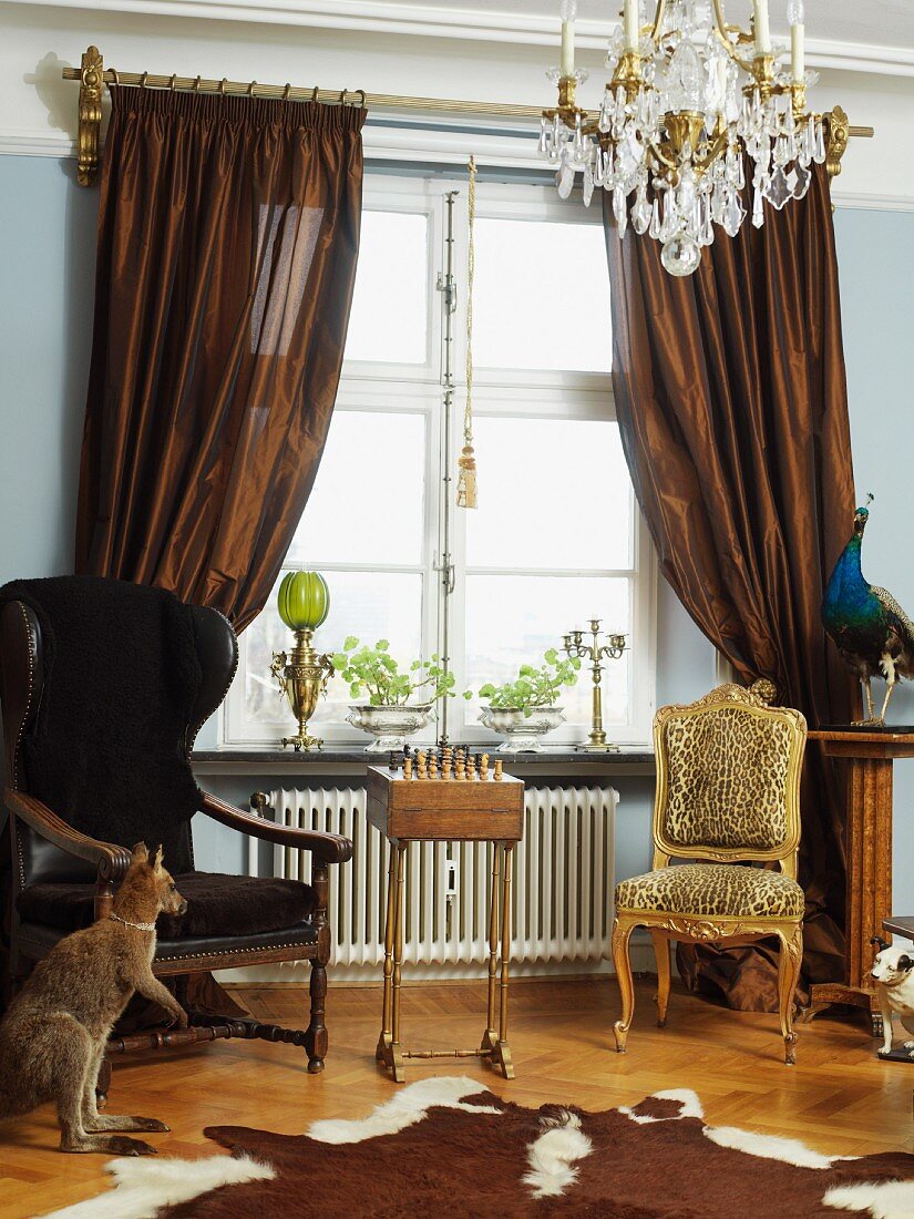 Wohnzimmer im Stilmix mit prunkvollem Kristallleuchter, barockem Leopardenstuhl und einem Tierfell als Teppich