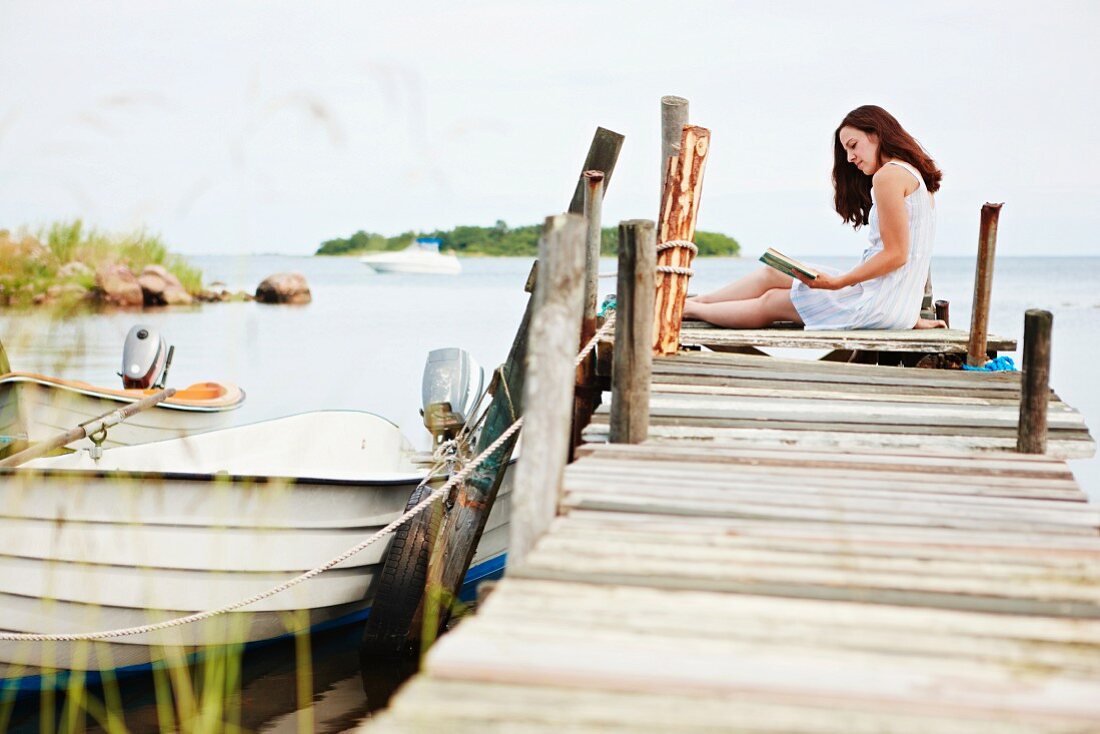 Woman sitting on jetty, reading book