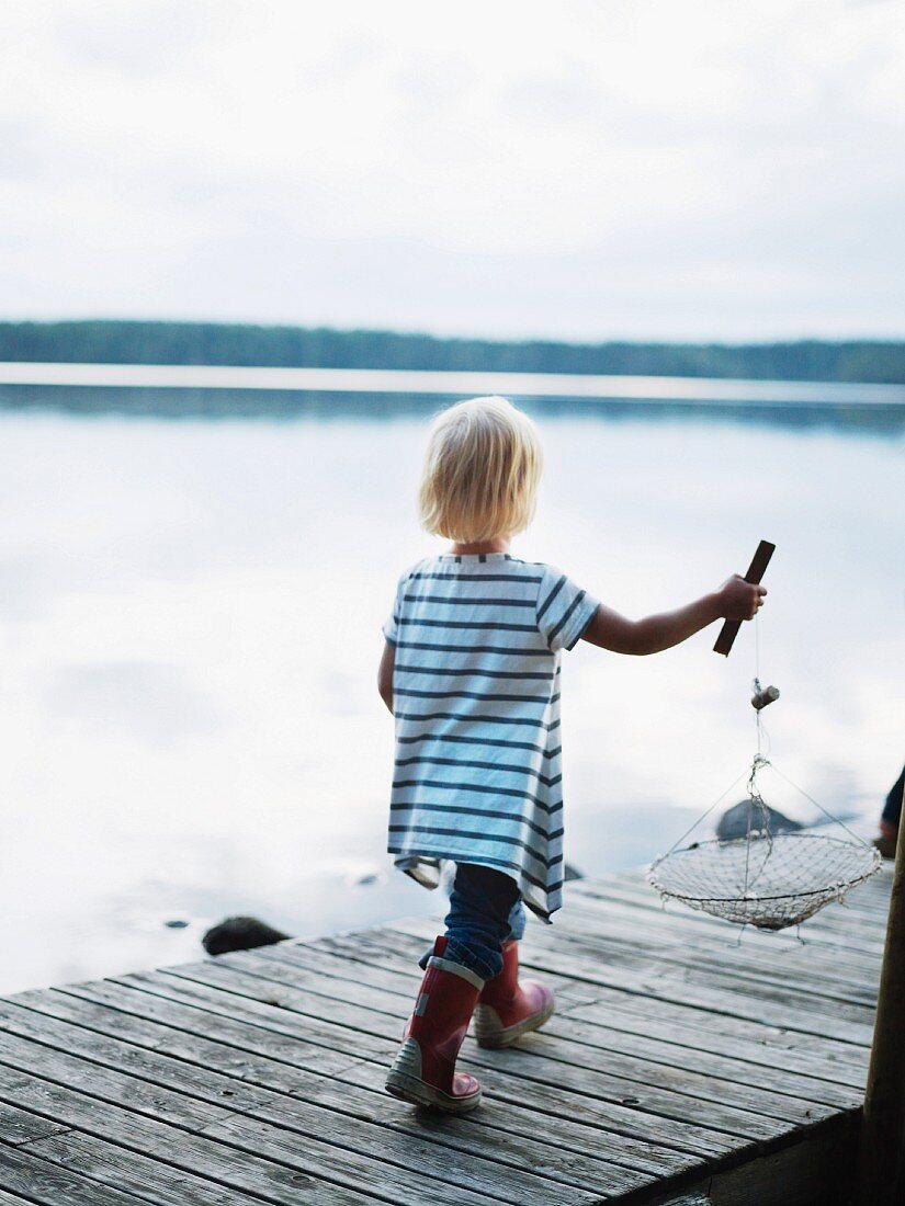 Kleines Mädchen mit Fischernetz auf einem Steg laufend