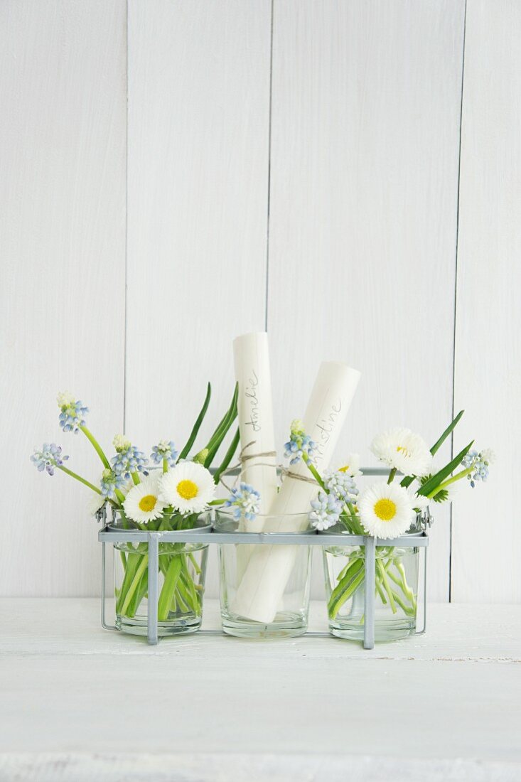 Glasses filled with grape hyacinths, bellis and names written on rolls of paper