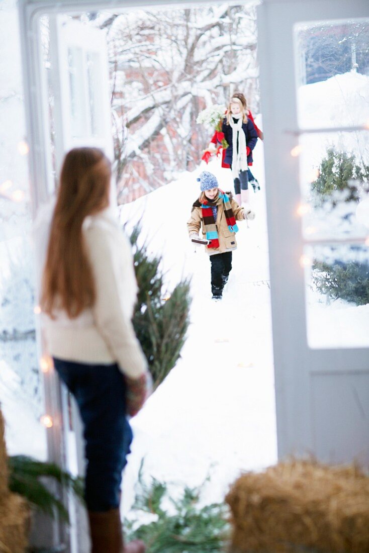 Mädchen in Tür stehend empfängt durch Schnee laufende Gäste