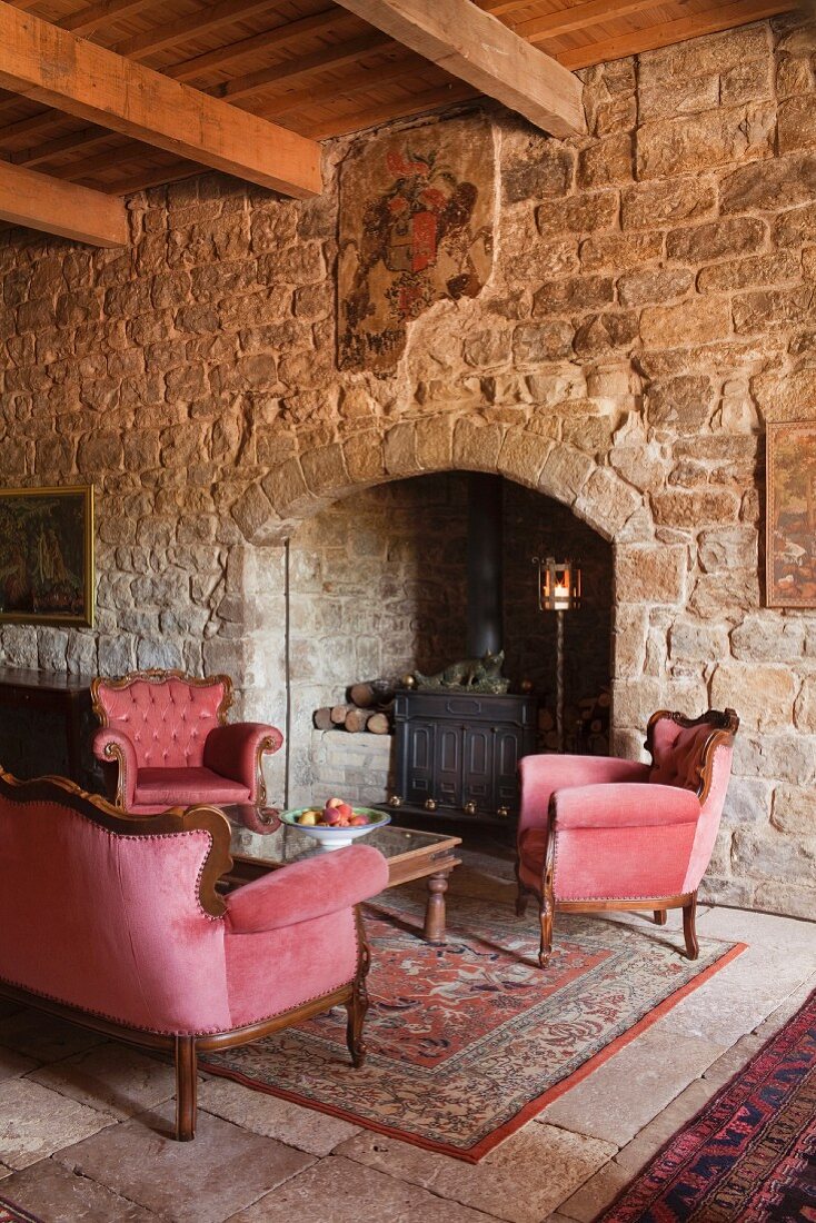 Room with stone walls, beam ceiling, fireplace and velvet sofa set in manor house (Languedoc, France)