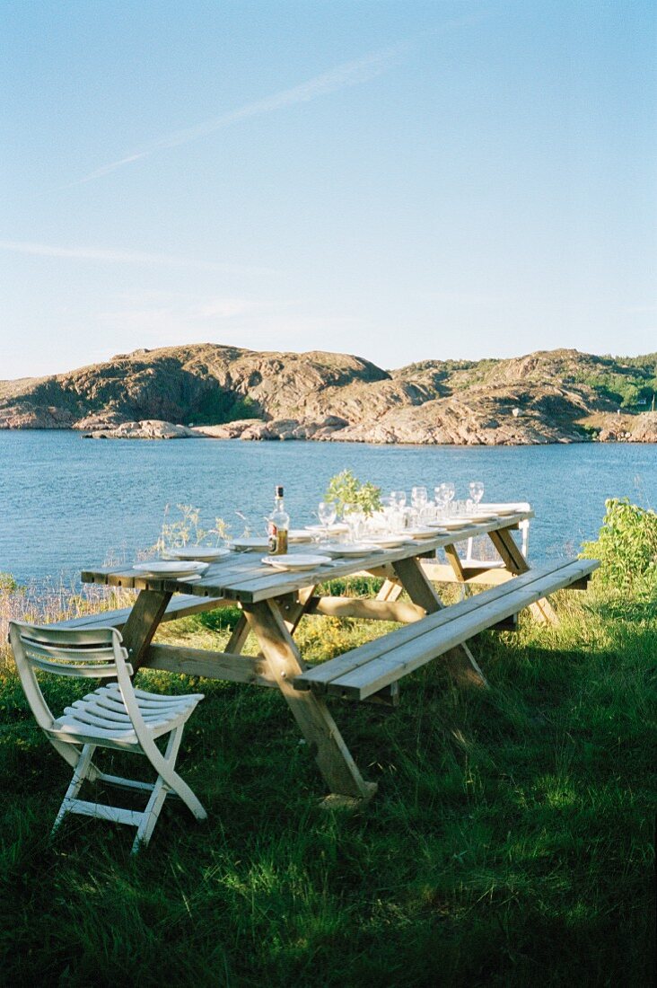 Set picnic table with benches & chairs in meadow with view of sea and mountain landscape
