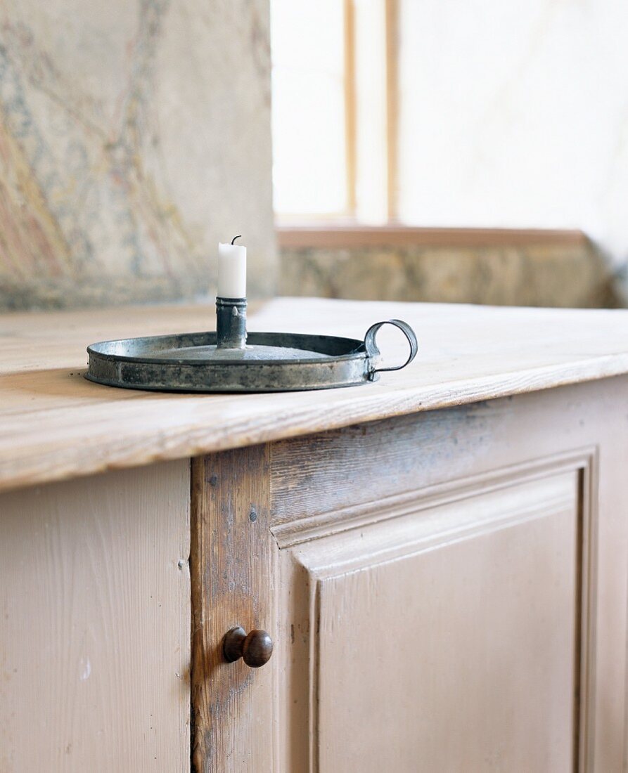 Candle in antique candlestick on wooden cabinet