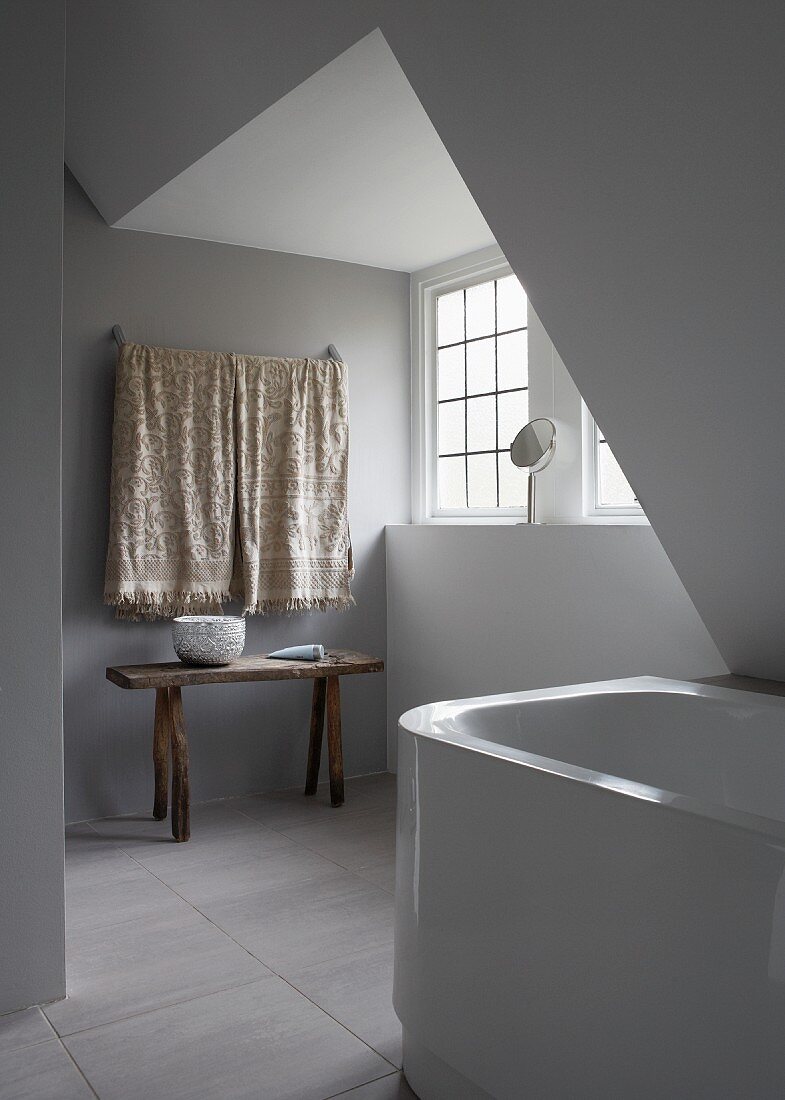 Minimalistisches Badezimmer mit rustikalem Wandtisch und Badewanne unter der Dachschräge