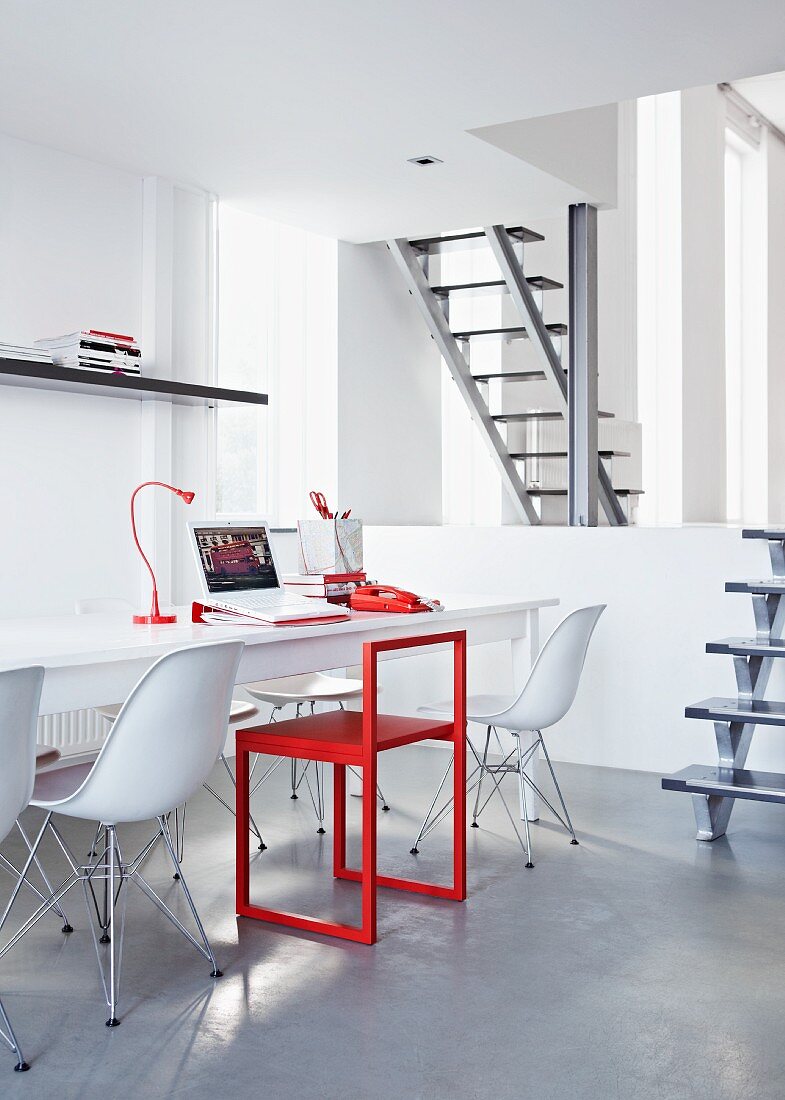 Arbeitsraum unter der Galerie in Weiß und Rot mit langem Arbeitstisch und weissen Eames-Stühlen