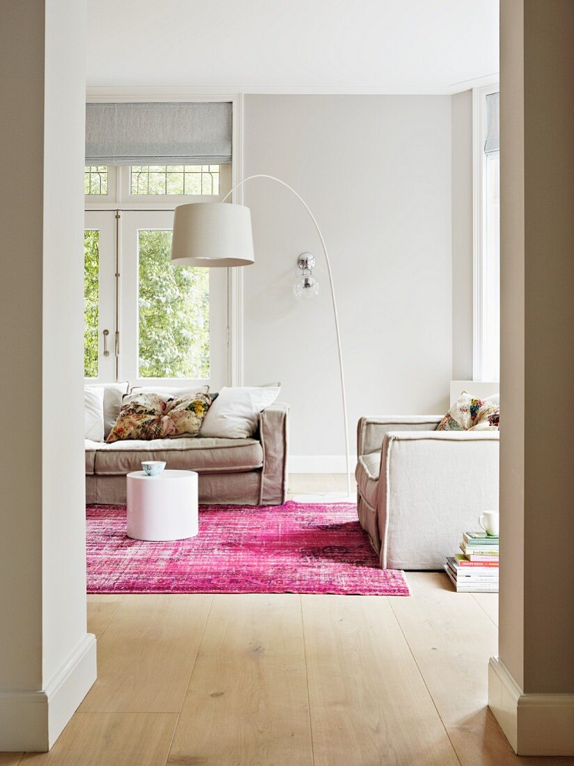 weiße Bogenlampe über grauer Wohnzimmercouch in hellem Wohnraum mit pinkfarbenem Teppich