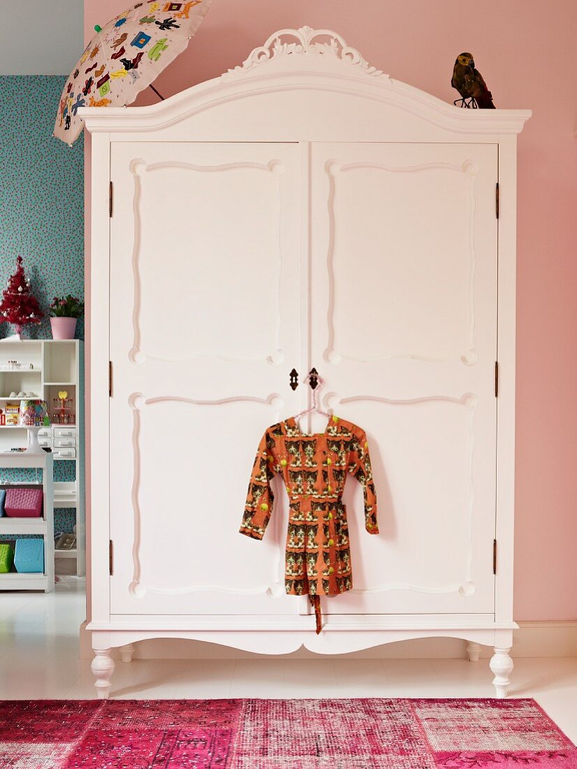 Weiß lackierter, antiker Kleiderschrank vor rosa Wand in Kinderzimmer