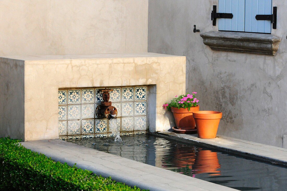 Betonierter Wasserlauf mit antikem Wasserspeier neben grauen Hauswand im Sonnenschein