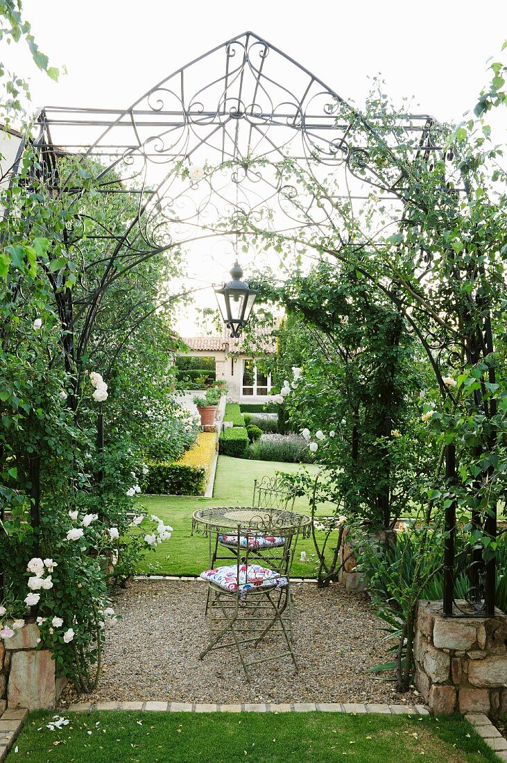 Idyllische Gartenlaube mit nostalgischer Rankhilfe und Rosen um den Sitzplatz in der Mitte