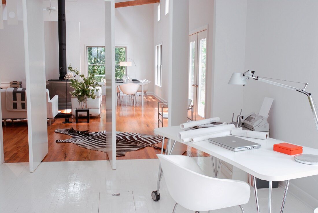 White, designer, retro-look workstation on white-painted wooden floor in front of open rotating partitions showing view of living room with zebra-skin rug on wooden floor