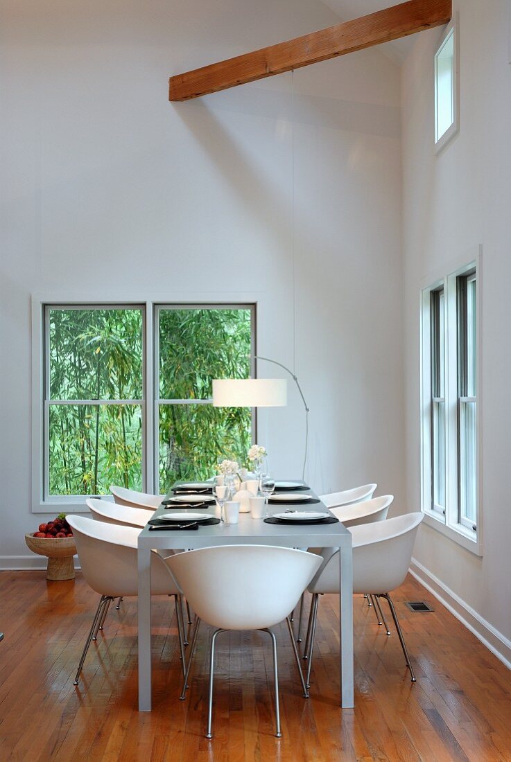 weiße Schalenstühle an gedecktem Tisch in minimalistischem Esszimmer vor Fenster