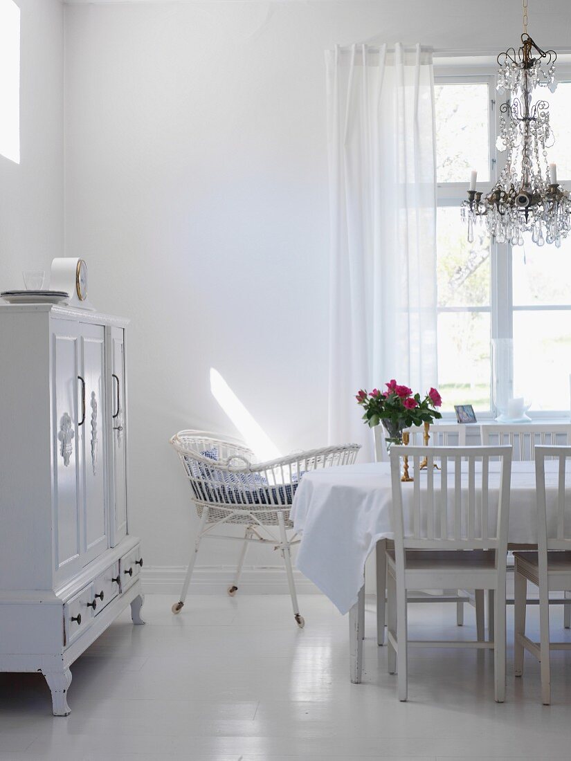 Wohnraum in Weiß mit Esstisch, Kronleuchter, Kinderbettchen & Buffetschrank