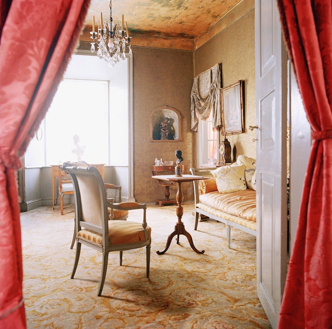 Blick durch geöffnete Tür mit Vorhängen in edlen Wohnraum mit Teppichboden, antiken Sitzmöbeln & Kronleuchter