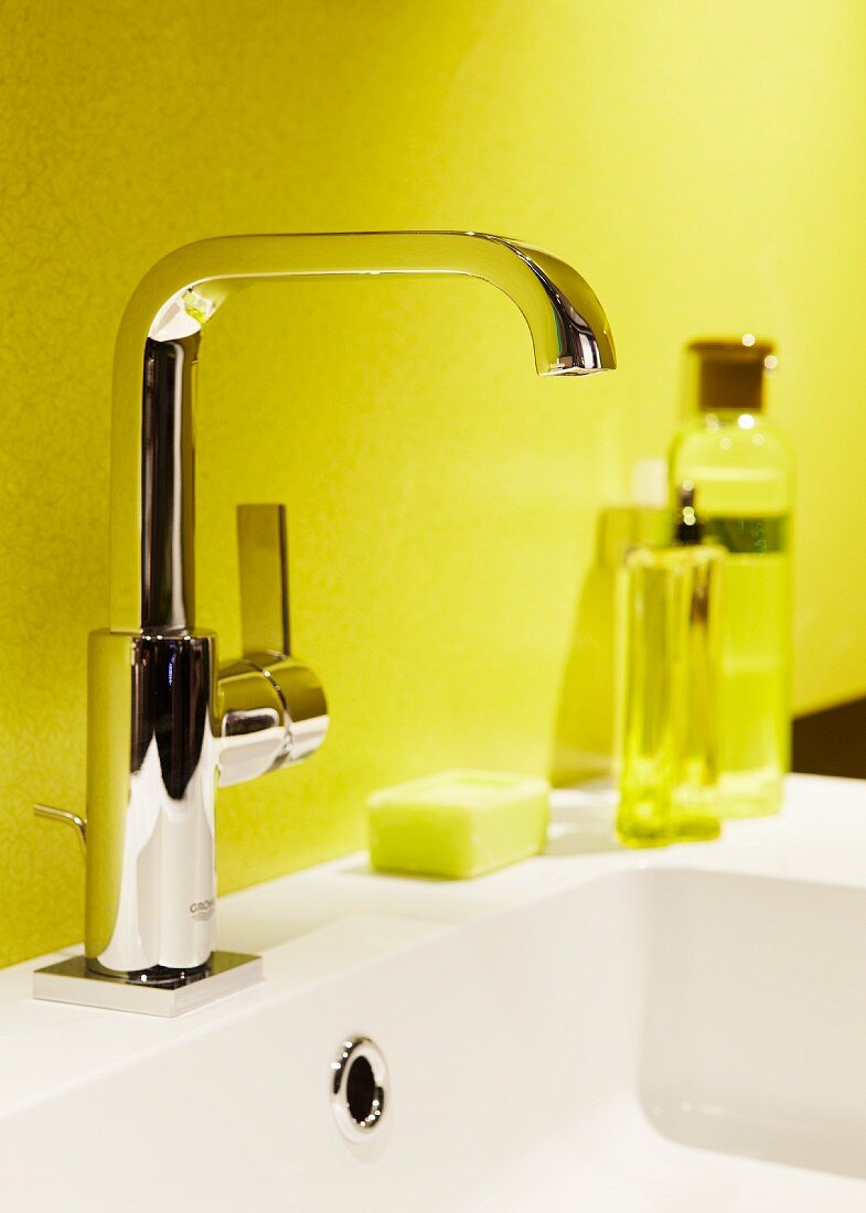 Glänzende Waschbeckenarmatur vor gelber Badezimmerwand