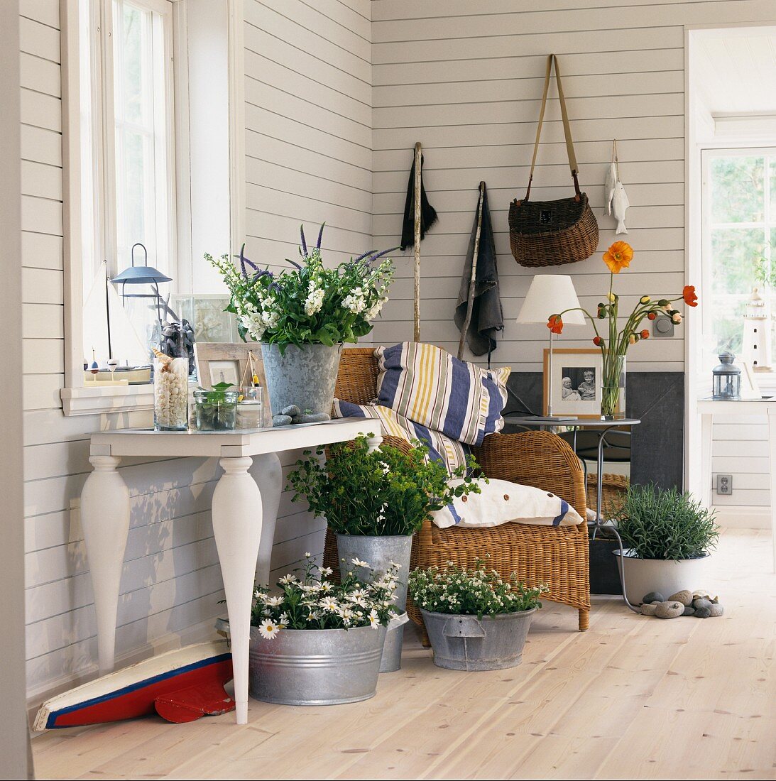 Various plants and bouquets in zinc containers, wicker chair and console table in white, wood-panelled country house