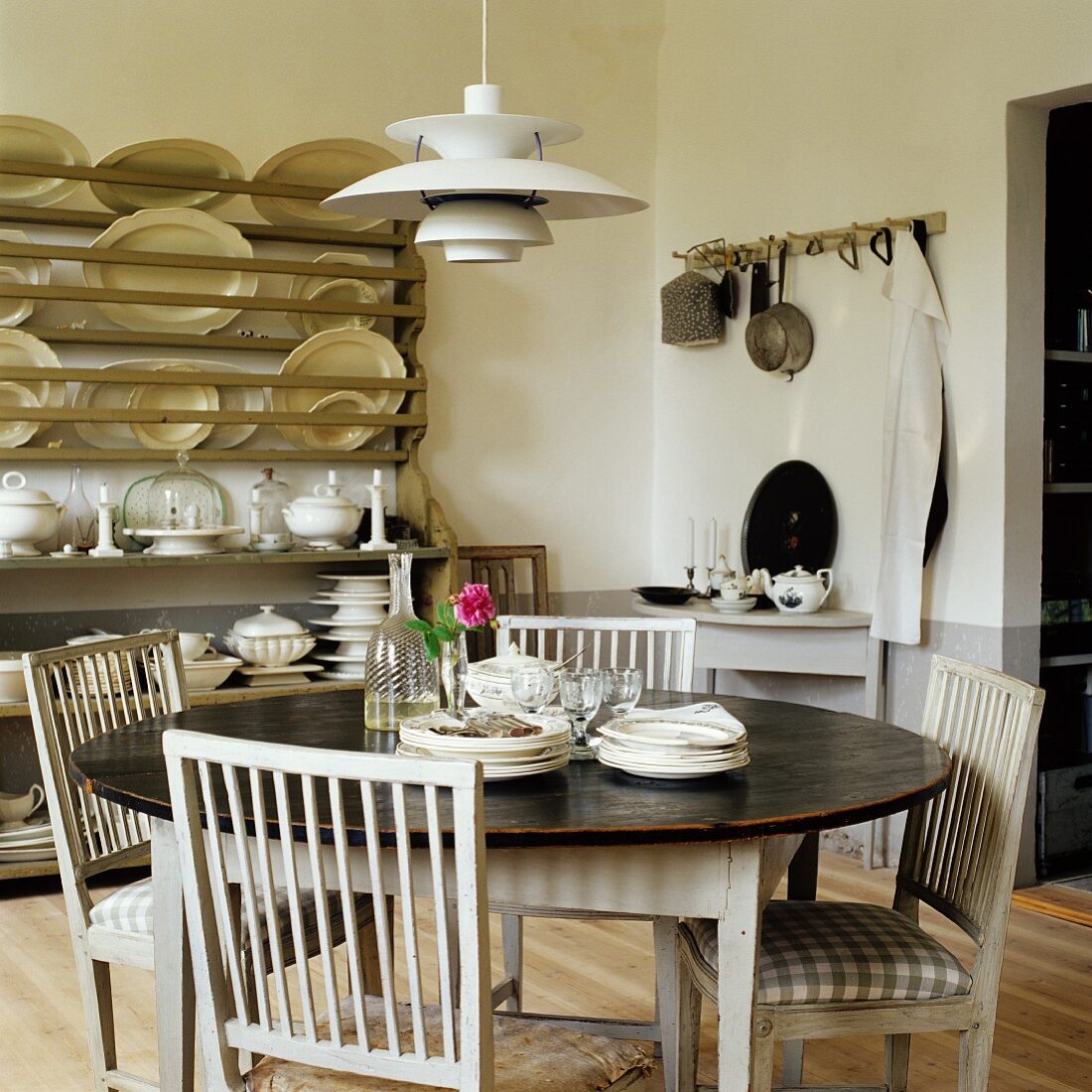 Round dining table, kitchen chairs with seat cushions and 50s, Danish designer lamp; plate rack in background