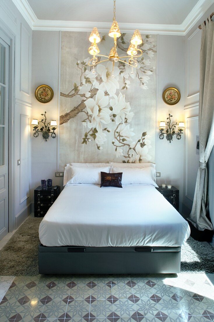Klassischer Schlafraum mit grossformatigem Blütenbild und schmiedeeisernen Lampen hinter Doppelbett
