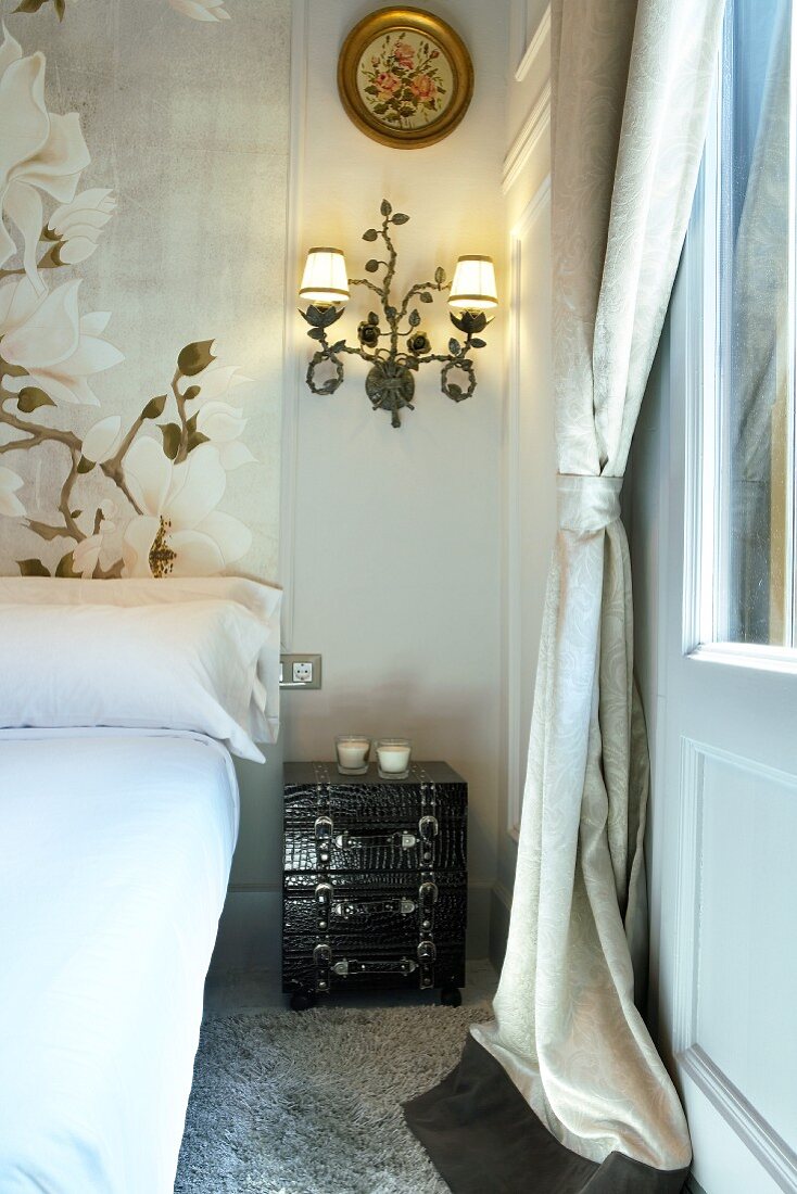 Nachttisch im Kofferdesign und schmiedeeiserne Wandlampe neben Bett