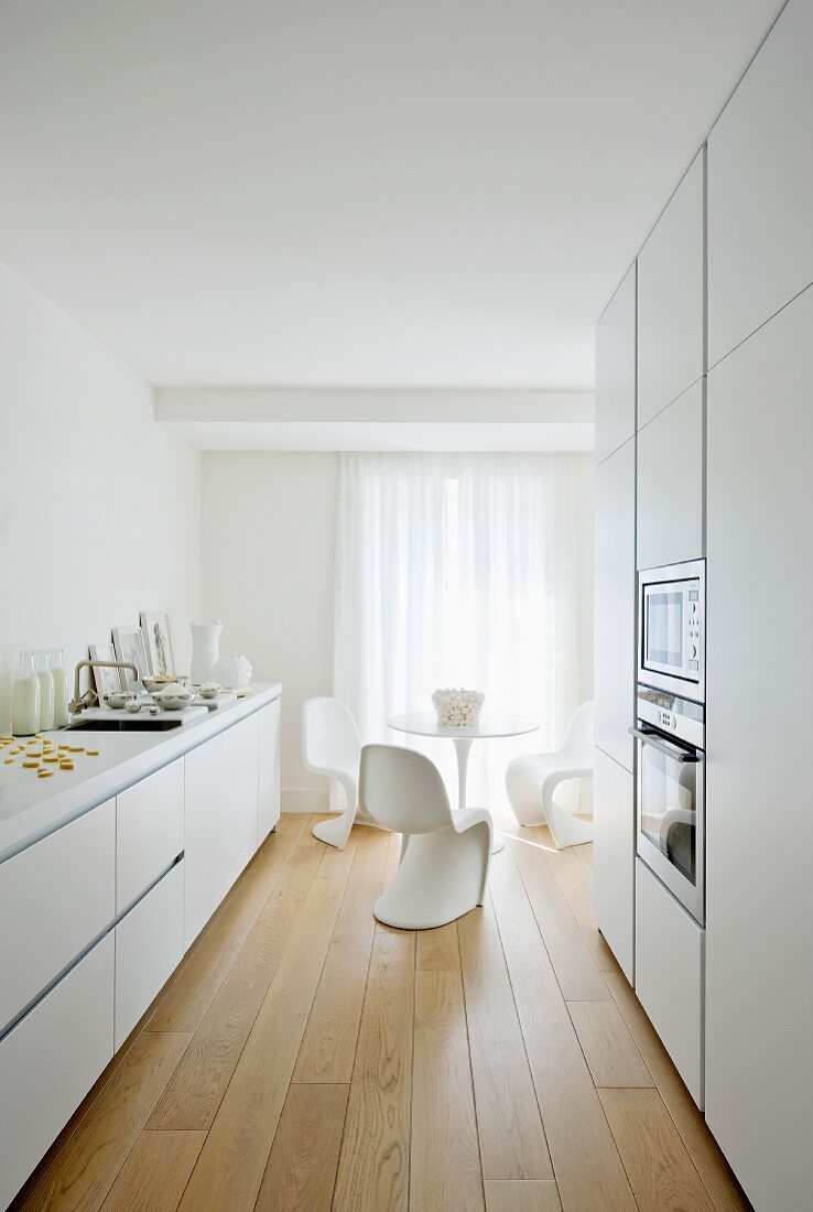 Elegant, white, designer kitchen with dining area in background