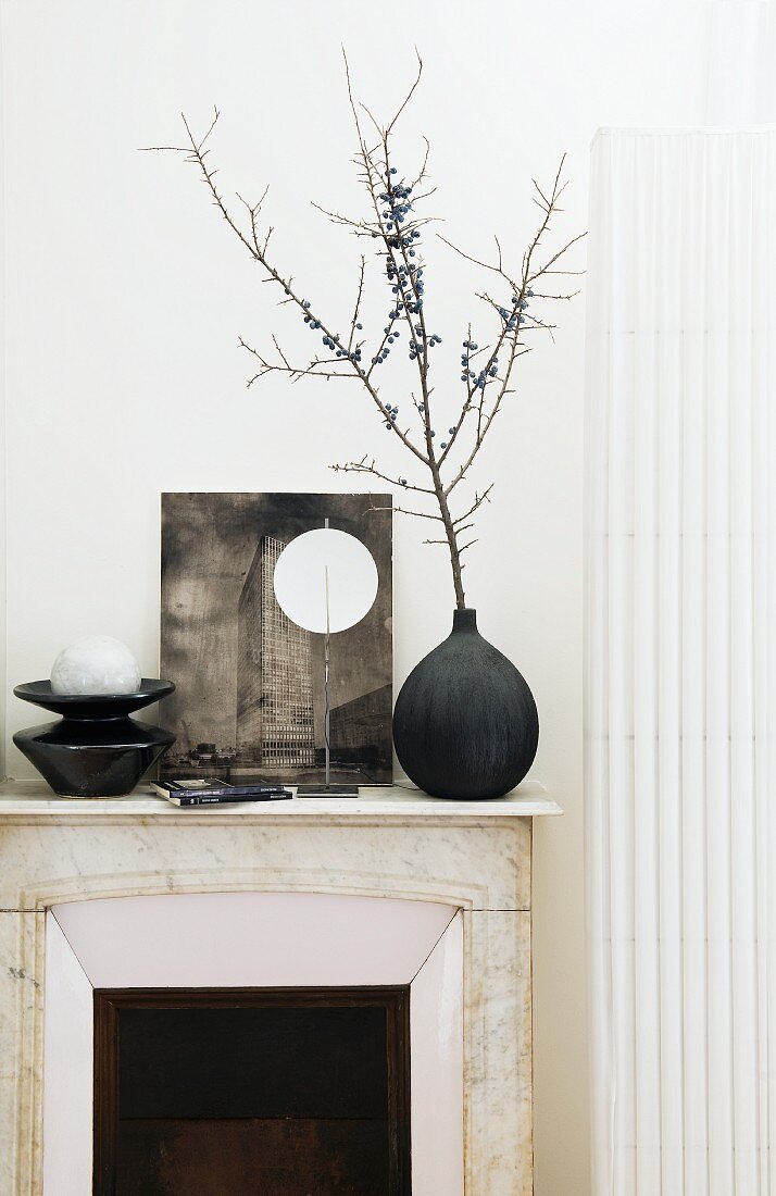 Black and white arrangement with vase and objet d'art on mantelpiece against white wall