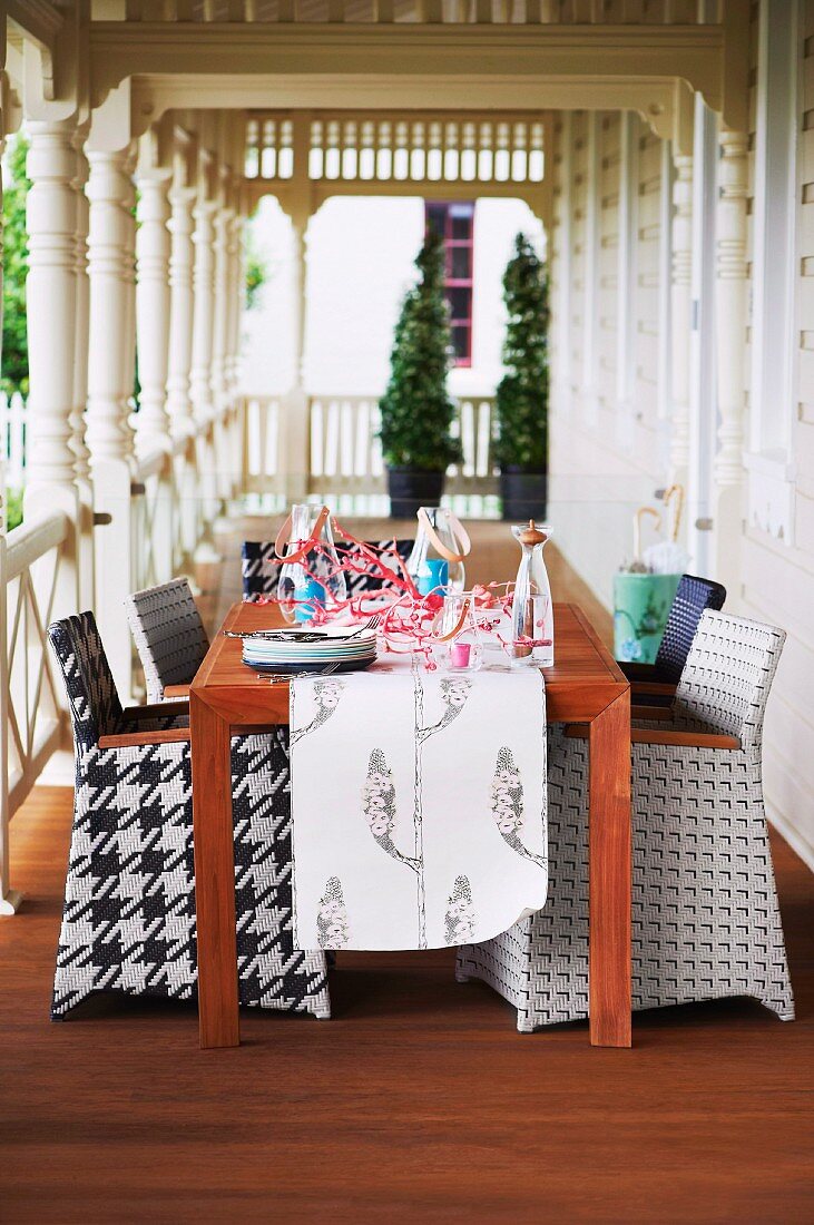 Chairs with graphic-patterned upholstery at wooden table on wooden veranda with turned pillars