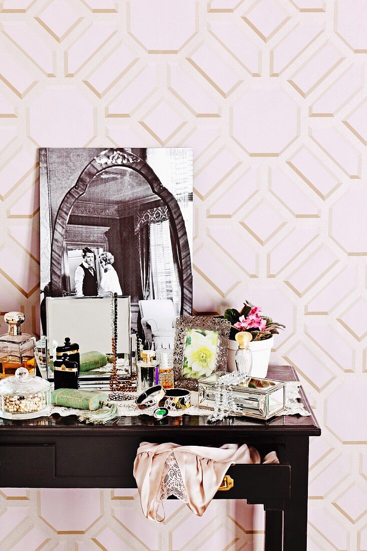 Cluttered dressing table with nostalgic black and white photo against pink, geometric wallpaper