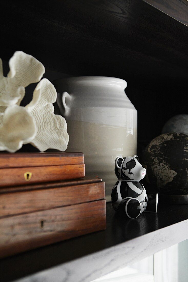 Zwei Holzschatullen mit weißer Muschel, Keramikvase und kleiner schwarz-weißer Bärenfigur auf scharzem Regalbrett