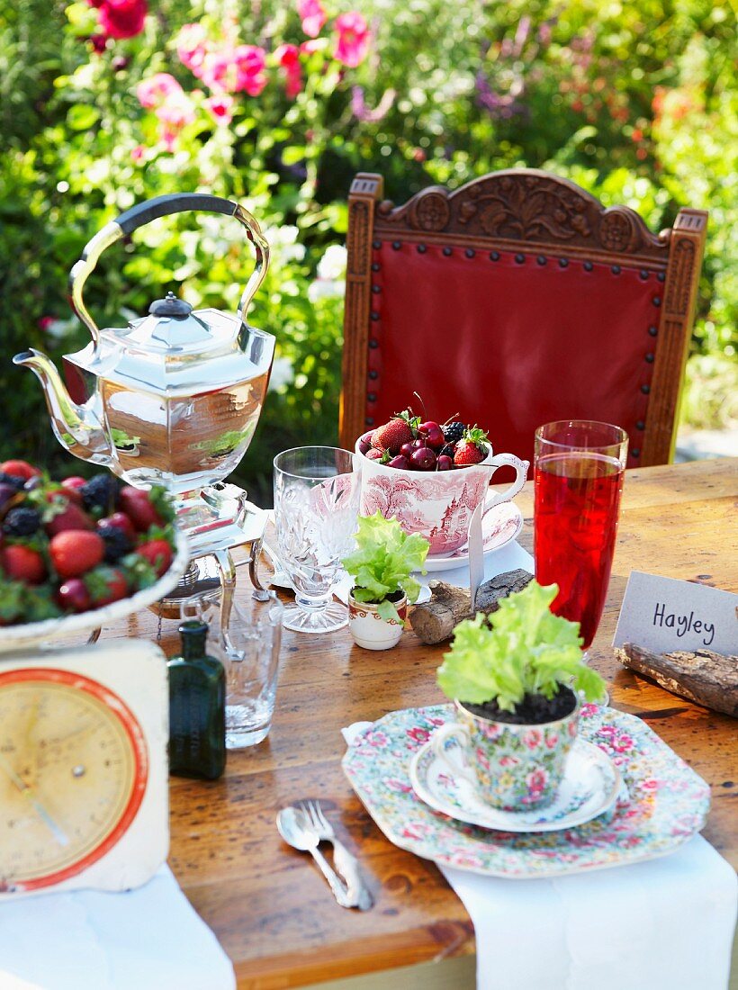 Gedeckter Tisch mit Beeren, Salatpflänzchen und Teekessel im Garten
