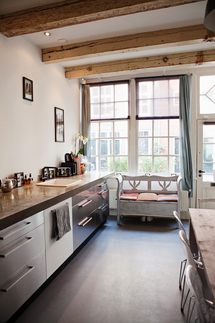 Küchenzeile mit Edelstahlfront und bäuerliche Sitzbank vor Sprossenfenster