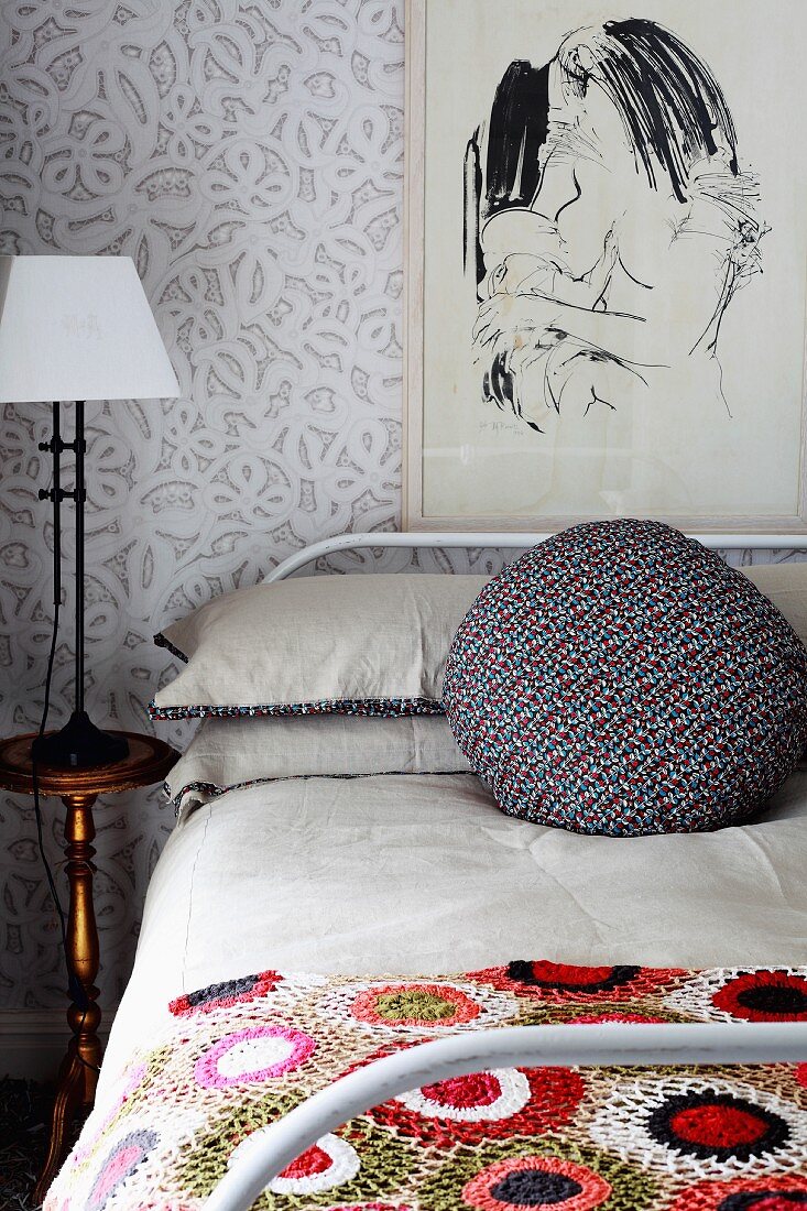 Schlafzimmer mit gehäkelter Bettdecke auf Bett, abstraktem Wandbild & Nachttischlampe