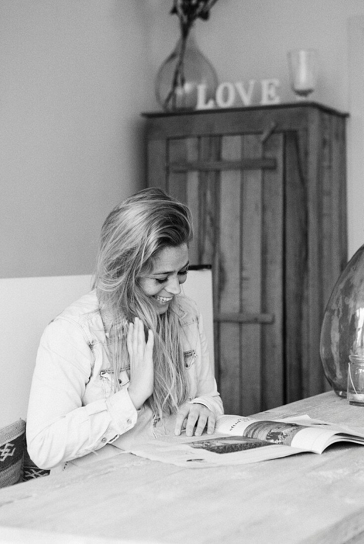 Junge Frau am Tisch beim Lesen einer Zeitschrift (s-w-Aufnahme)