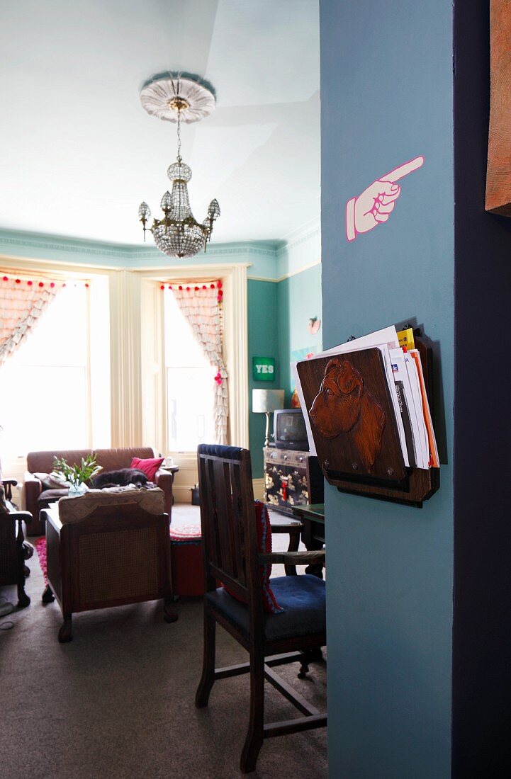 Blick in Erkerzimmer mit Polstermöbel, blau gestrichener Wandpfeiler mit Zeitschriftenhalter vom Flohmarkt