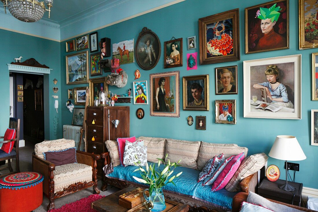 Various framed pictures of women on turquoise wall in crammed, vintage-style period apartment