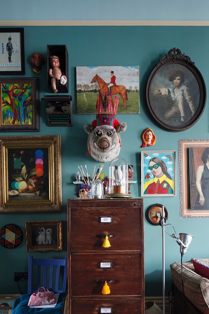 Hotchpotch of framed pictures and flea market finds on turquoise living room wall